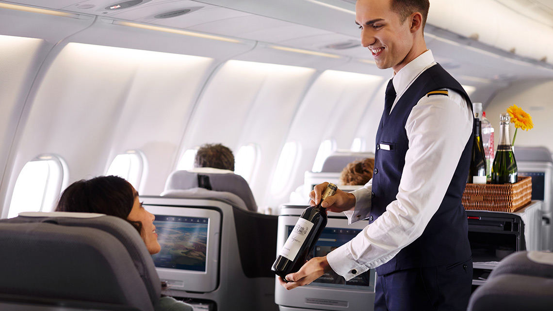 Ein Cabin Crew Mitarbeiter präsentiert einem Fluggast eine Flasche Wein