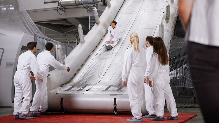 Participants of a Safety and Emergency Procedure Training practice the use of a rescue slide on a simulator