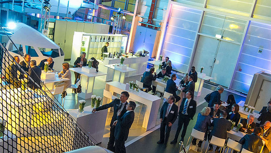 In a colourfully illuminated training centre there are bar tables and stools between the training equipment and around 30 guests