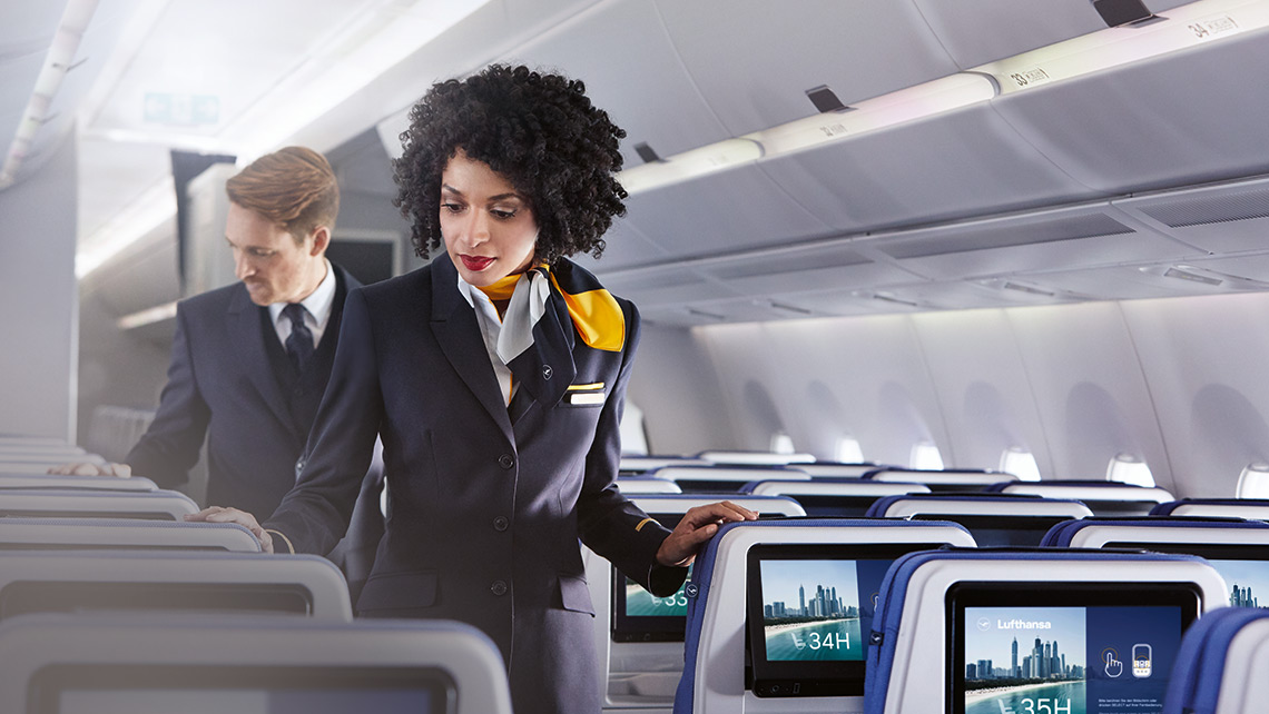 Two cabin crew members check the rows of seats in an aircraft without passengers