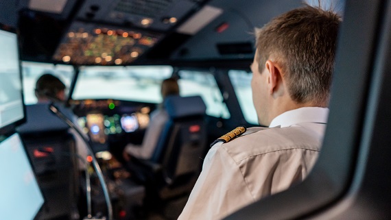 2 pilots sitting in a cockpit of an aircraft simulator with a trainer