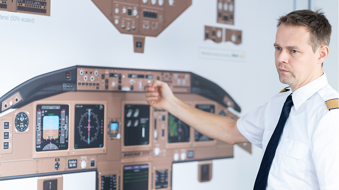 A pilot stands in front of a board showing an aircraft cockpit