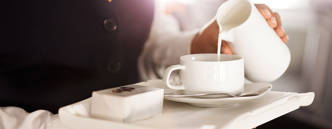 Close-up of a tray in the hands of a flight attendant pouring milk into a cup of coffee