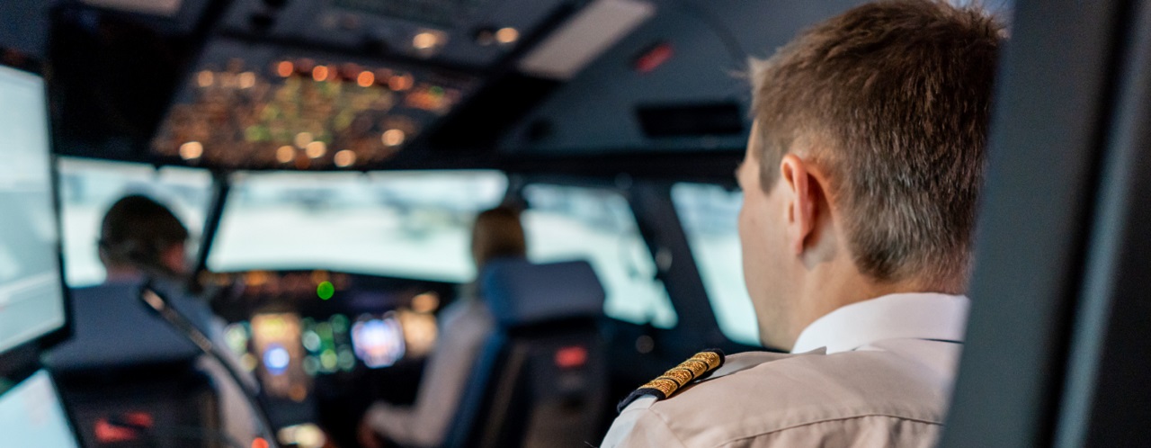 2 pilots sitting in a cockpit of an aircraft simulator with a trainer