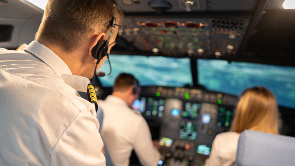 A pilot as trainer with headphones watches two pilots during a training in a cockpit simulator