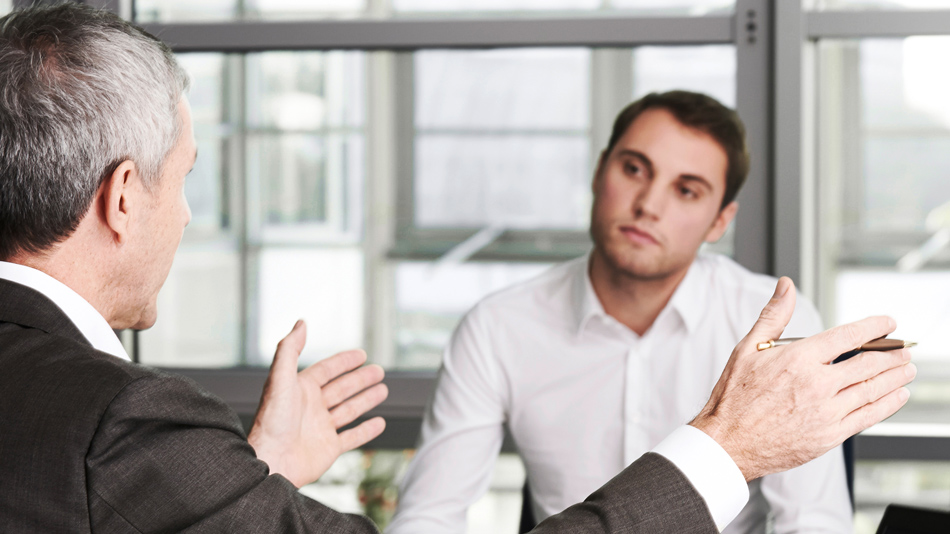 An older man in a suit explains something to a younger man