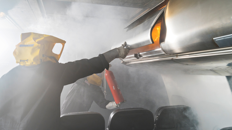 2 flight attendants wearing breathing masks train fire fighting in an aircraft cabin with fire extinguishers