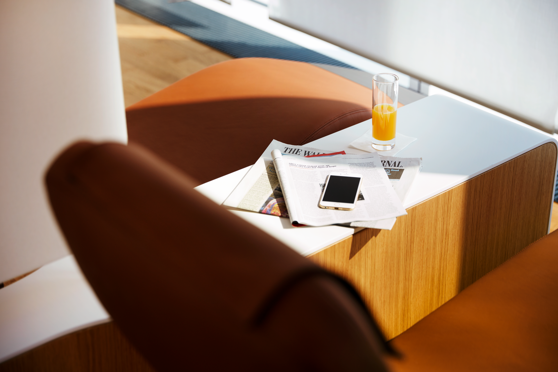Auf einem Tisch liegen eine Zeitung, eine Zeitschrift und darauf ein Handy, daneben steht ein Glas Orangensaft.