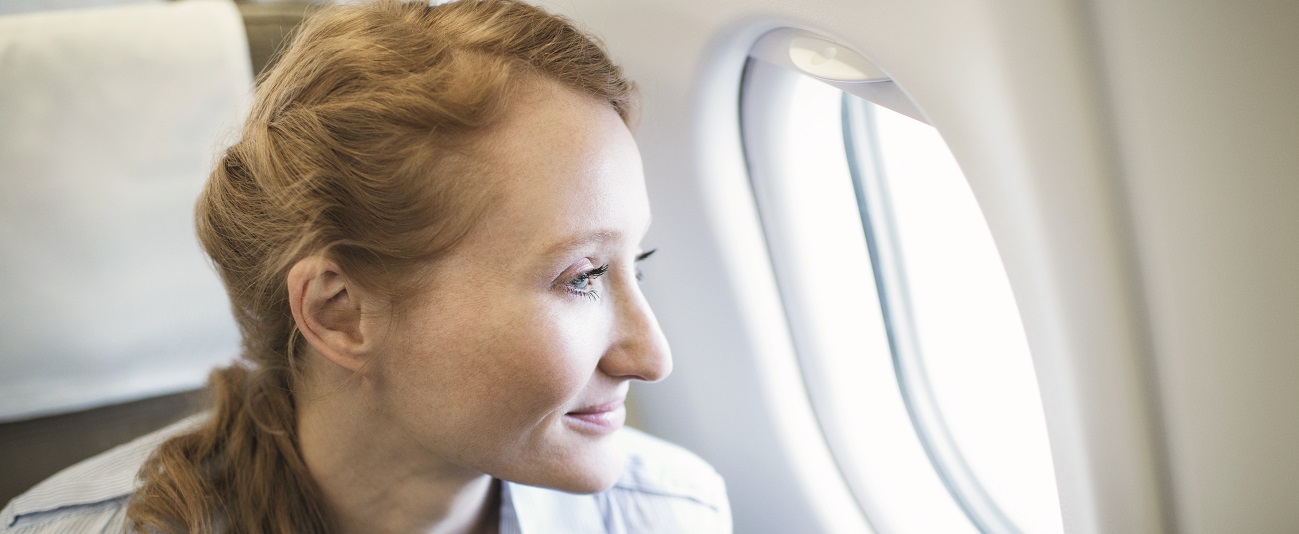 Eine Person sitzt in einem Flugzeug auf dem Fensterplatz und blickt aus dem Flugzeugfenster.