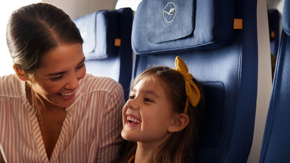 Eine Mutter mit Kind sitzen nebeneinander im Flugzeug und lachen.