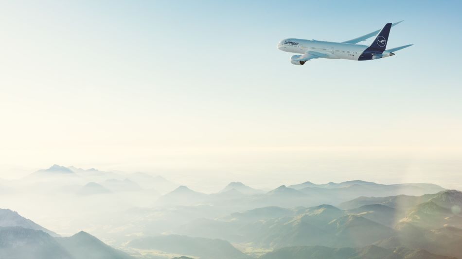 Ein Flugzeug der Airline Lufthansa fliegt über eine Hügellandschaft.