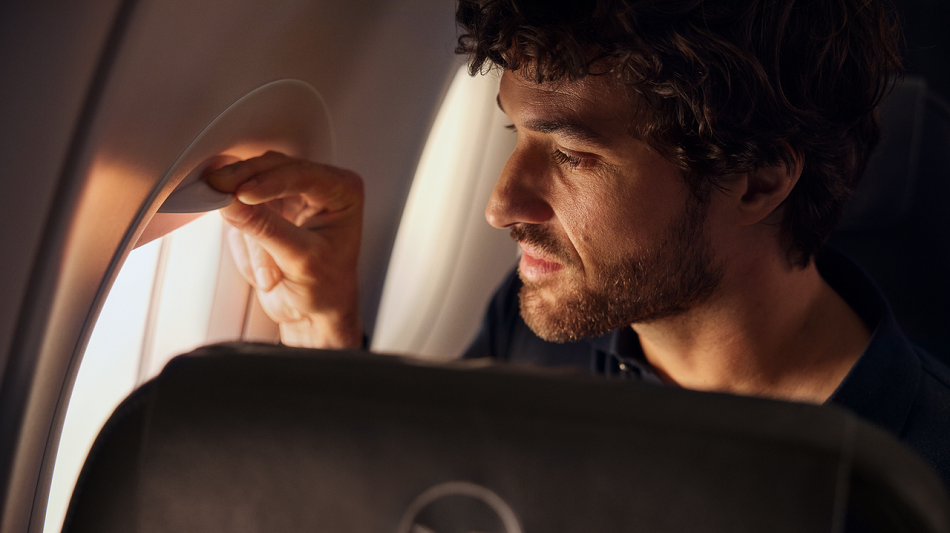 Eine Person mit Flugangst sitzt in einem Flugzeug am Fenster und blickt aus dem Fenster.