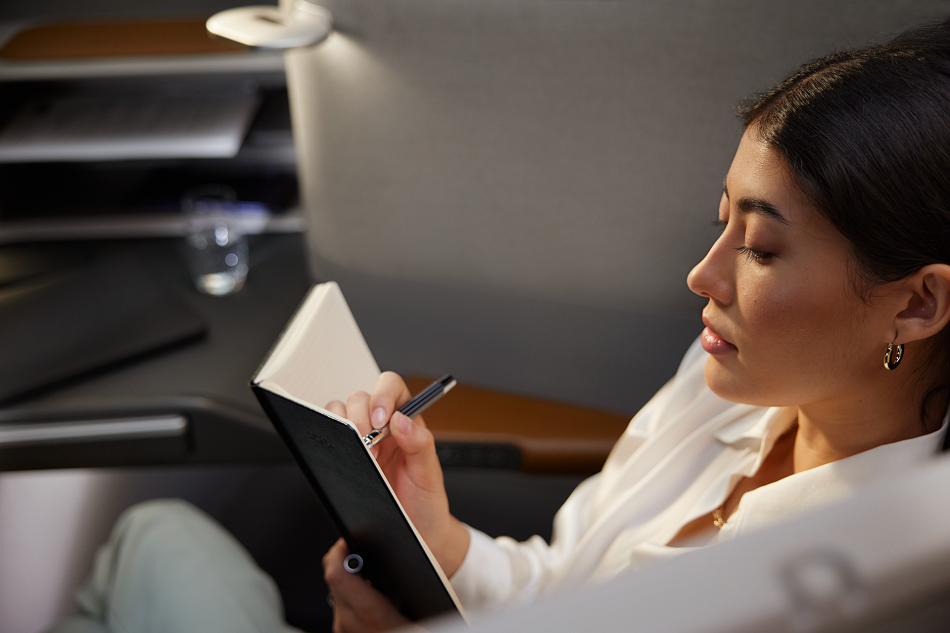 Eine Person sitzt in einem Flugzeug und schreibt in ein Notizbuch Tipps gegen Flugangst.