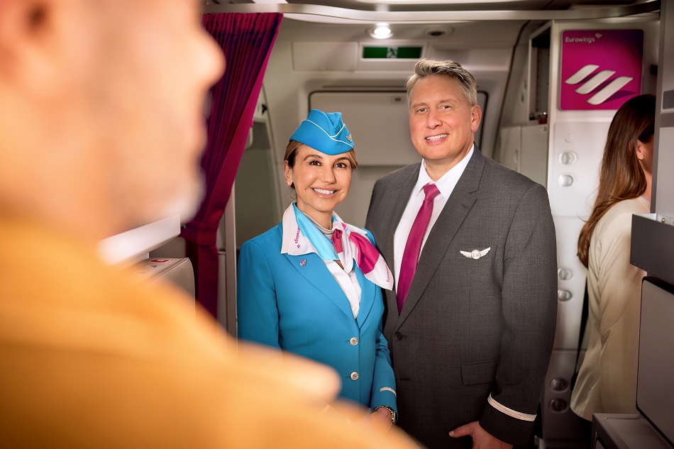 Zwei Flugbegleiter:innen stehen an der Tür eines Flugzeugs und begrüßen die einsteigenden Passagiere.