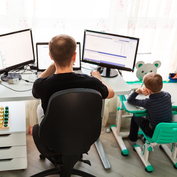 An adult and a child are sitting next to each other at separate desks, working.